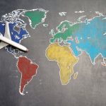 World Adventure - Top view of crop anonymous person holding toy airplane on colorful world map drawn on chalkboard