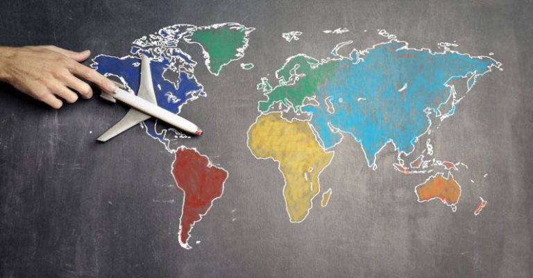World Adventure - Top view of crop anonymous person holding toy airplane on colorful world map drawn on chalkboard
