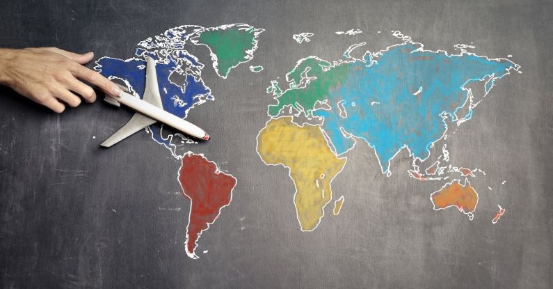 World Adventure - Top view of crop anonymous person holding toy airplane on colorful world map drawn on chalkboard