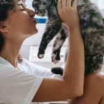 Pets Love - Charming woman kissing cute cat in bedroom