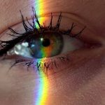 Creative Mind - Closeup of crop anonymous sad female with green eyes and rainbow light on face looking at camera