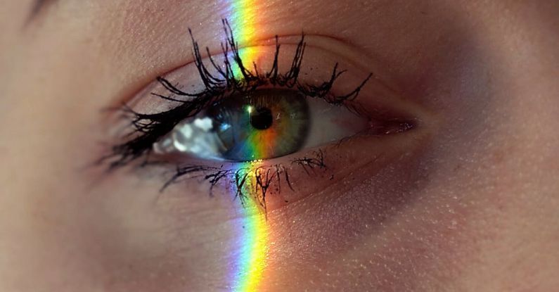 Creative Mind - Closeup of crop anonymous sad female with green eyes and rainbow light on face looking at camera