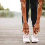 Sports Sneakers - From below crop slender female athlete in sportswear and white sneakers doing standing forward bend exercise for stretching body on wooden floor of street sports ground against blurred urban environment in daytime
