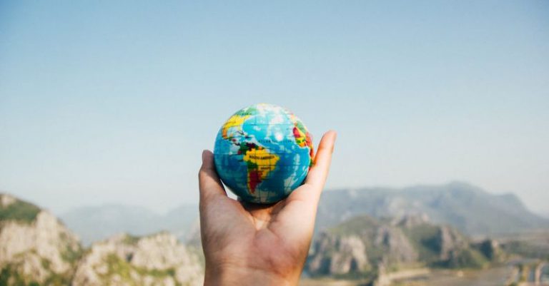 World Travel - Person Holding World Globe Facing Mountain