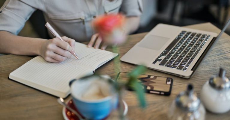 Content Creation - Person Writing On A Notebook Beside Macbook