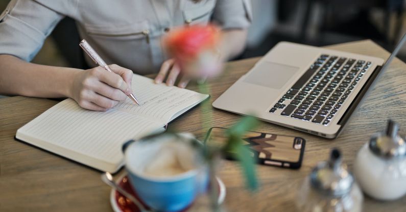 Content Creation - Person Writing On A Notebook Beside Macbook