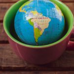 Facemask Globe - A small globe sitting in a cup on a wooden table